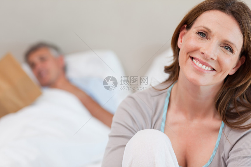 在床上微笑的成年妇女 在她身后与阅读丈夫在一起图片