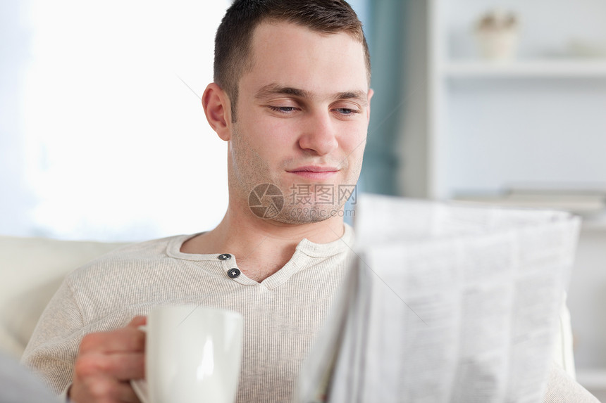 笑脸男人在看新闻时喝咖啡白色沙发闲暇报纸阅读生活年轻人住房长椅饮料图片