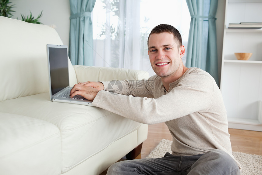 用笔记本电脑坐在地毯上微笑的男人图片
