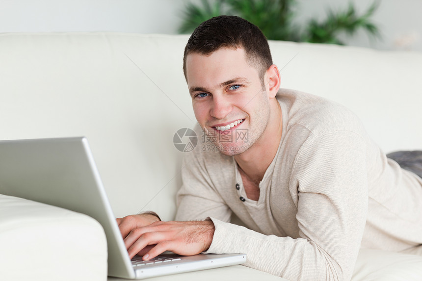 男人用笔记本电脑躺在沙发上房间电子邮件微笑冲浪闲暇说谎房子生活腹部沟通图片