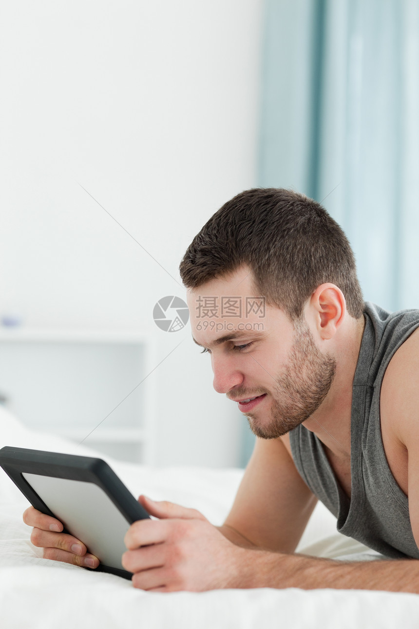 一名青年男子躺在h上时使用平板电脑的肖像图片