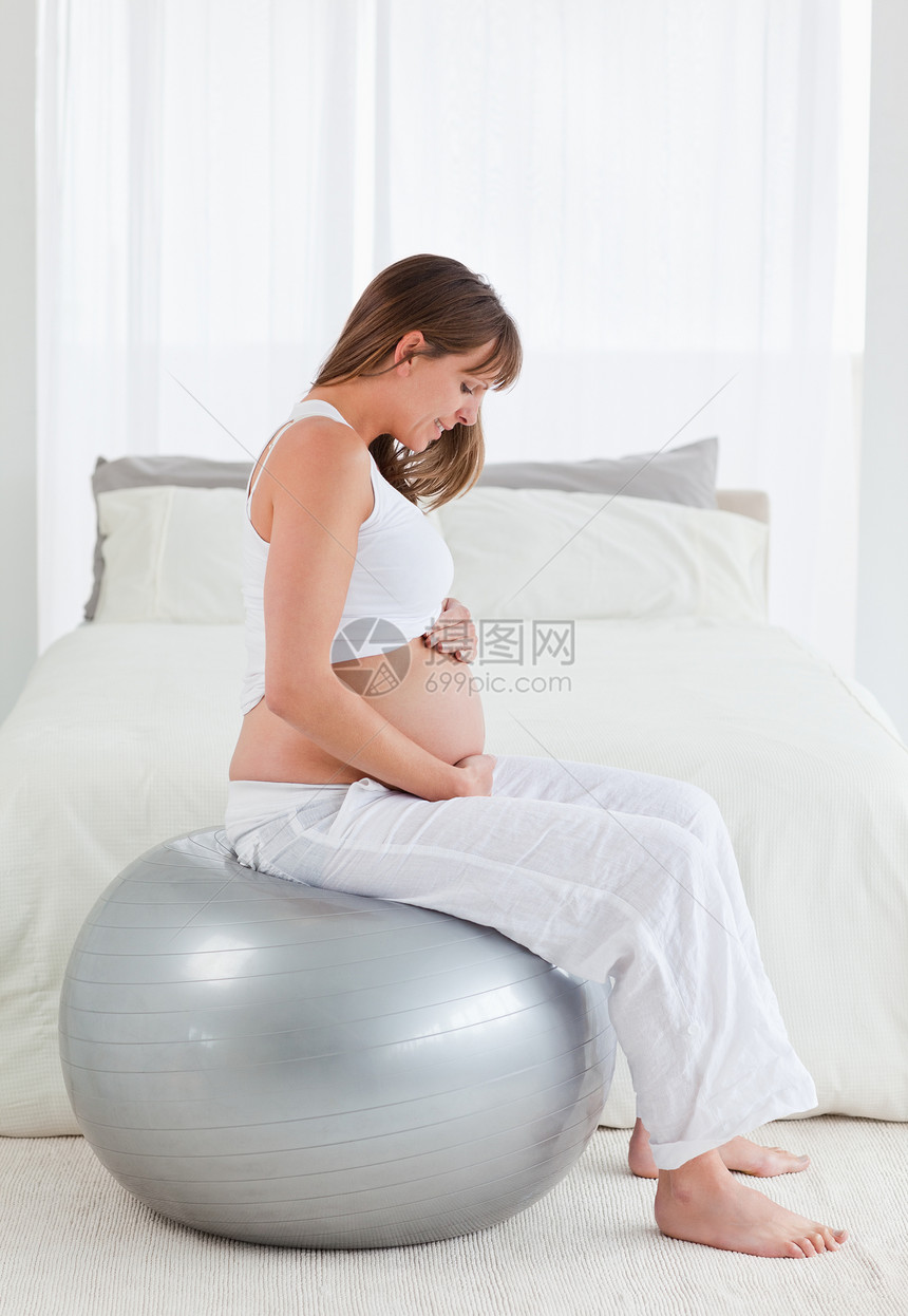 看着漂亮 怀孕的孕妇在坐着时抚摸她的肚子卧室练习气球女性婴儿腹部亮度女士窗帘健身房图片