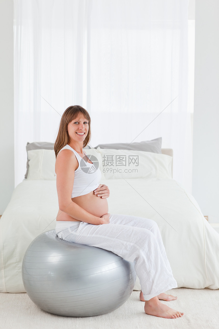 美丽的怀孕女孕妇坐着时抚摸她的肚子腹部女士气球亮度婴儿练习卧室健身房女性窗帘图片
