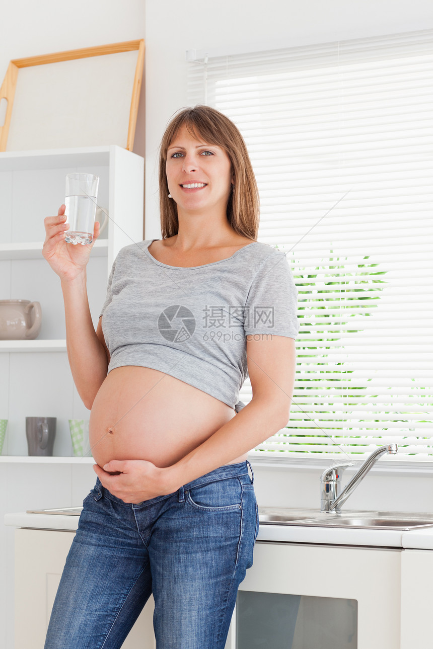 有吸引力的孕妇在站立时拿着一杯水喝着图片