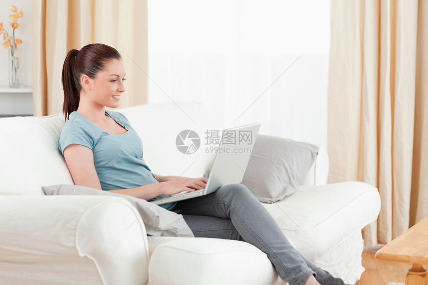 迷人的女人坐在沙发上用笔记本电脑放松图片