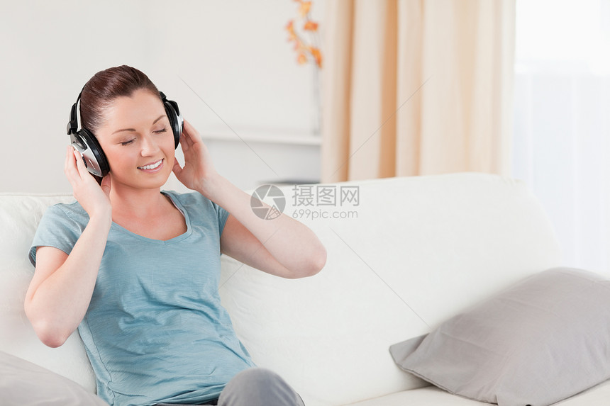 迷人的女人坐在沙发上 用耳机轻松放松图片