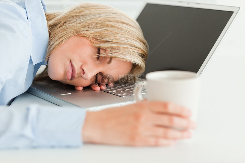 美丽的女人睡在笔记本电脑上 手拿着一杯咖啡图片