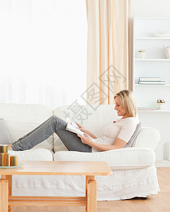妇女阅读杂志的肖像思维裙子冒充金发女郎微笑喜悦乐趣房子身体沙发背景图片
