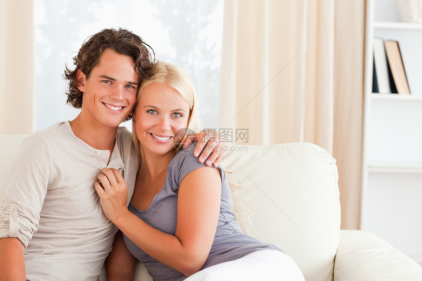坐在沙发上的一对幸福的情侣微笑夫妻喜悦男人房间拥抱商业金发女郎成人年轻人图片