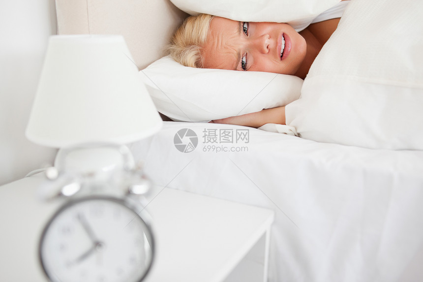 疲倦的女人把她的头藏在枕头里 当闹钟响起的时候图片