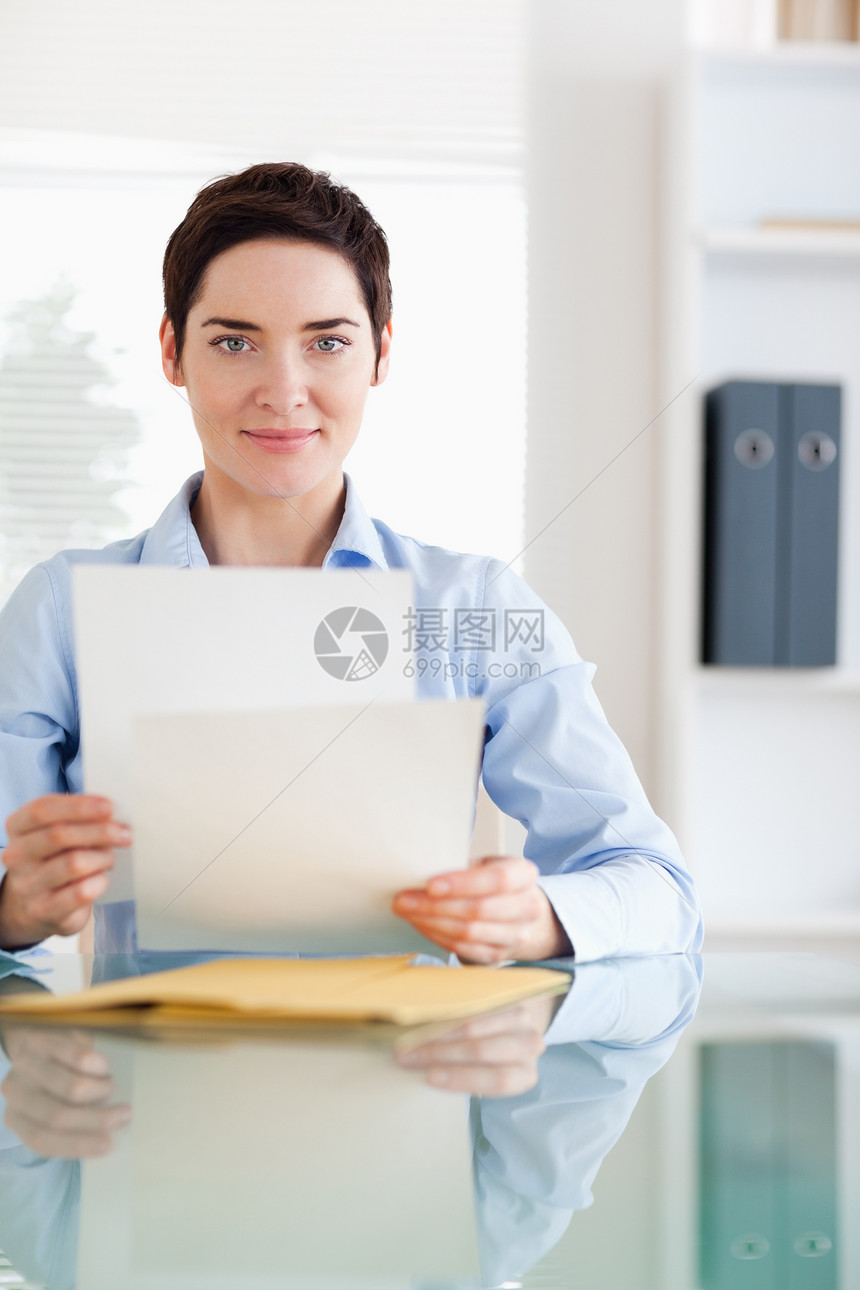 一名商业妇女坐在有文件的办公桌后面的肖像图片