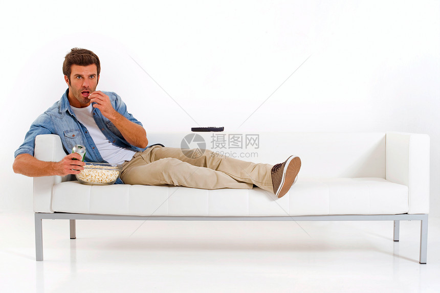 单身男子在沙发上看电视爆米花长椅小吃休闲装牛仔裤客厅男人专注成年人成人图片