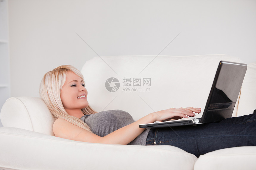 美丽的女人躺在沙发上的笔记本电脑上放松图片