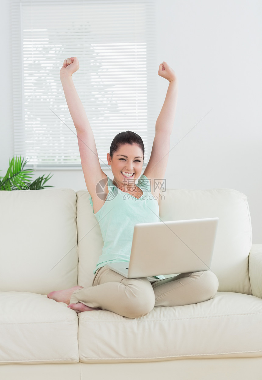 女人用笔记本电脑在沙发上举起手来女士胜利棕色家庭女性百叶窗成功客厅窗户房子图片