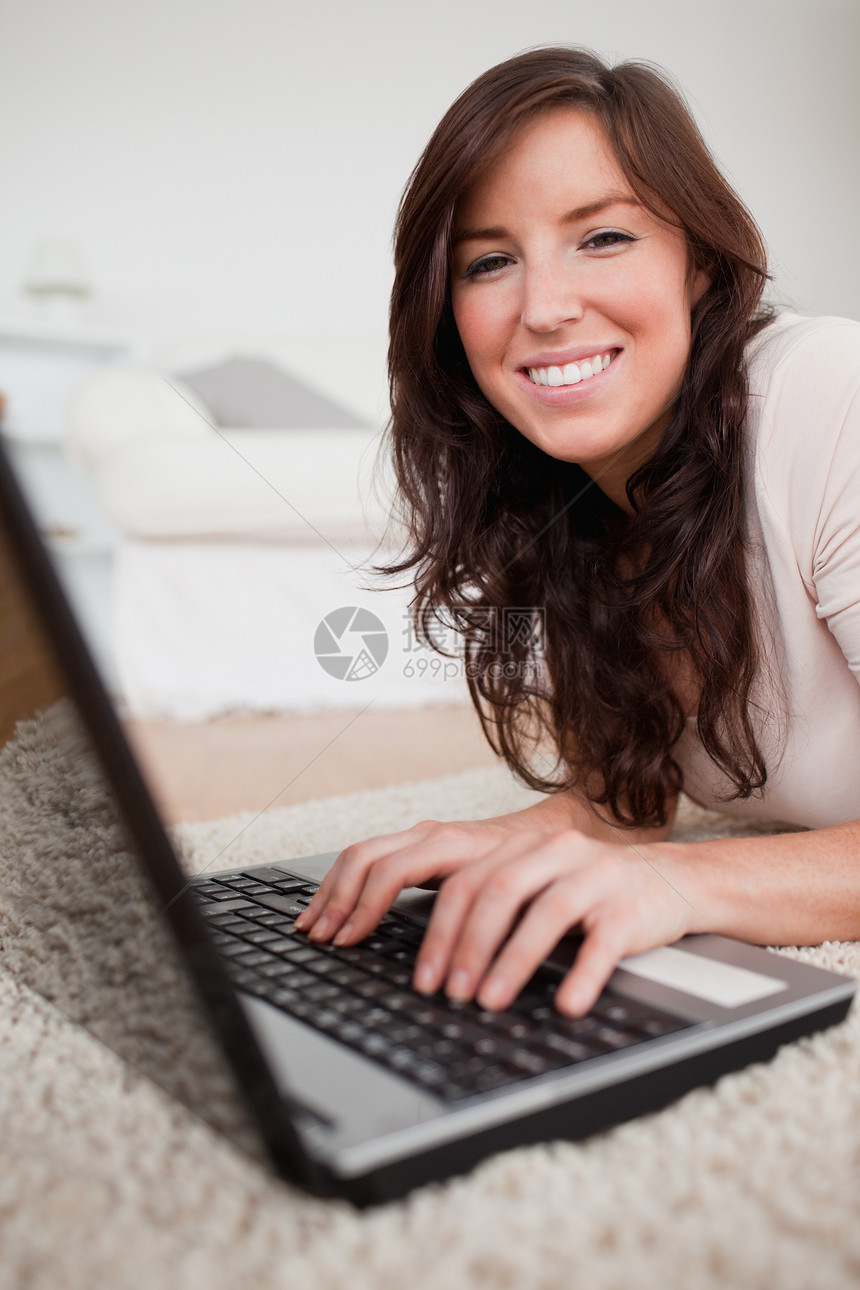 美丽的黑发女人在躺着时 用笔记本电脑放松图片