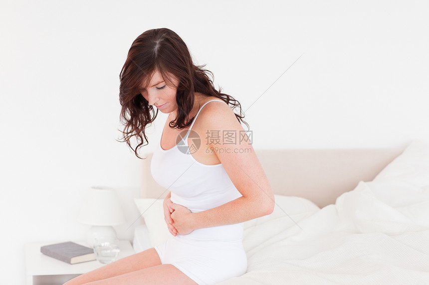 迷人的黑发美女坐着肚子痛得要命女孩母亲治疗药品卧室内饰女士制药女性图片