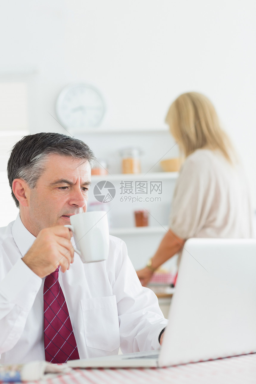 男人在检查膝上型电脑时喝咖啡图片