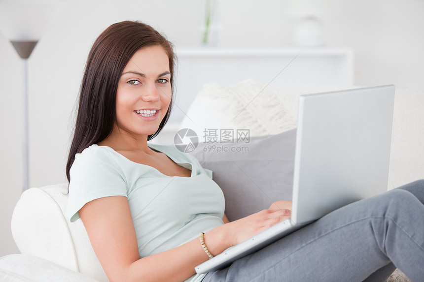 美丽的女人坐在沙发上时 用笔记本电脑打字图片