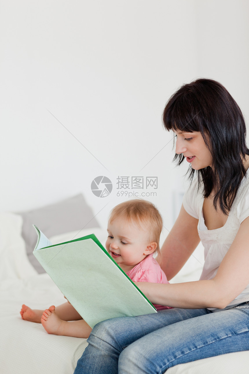 可爱的黑褐色女人坐着给婴儿看一本书图片