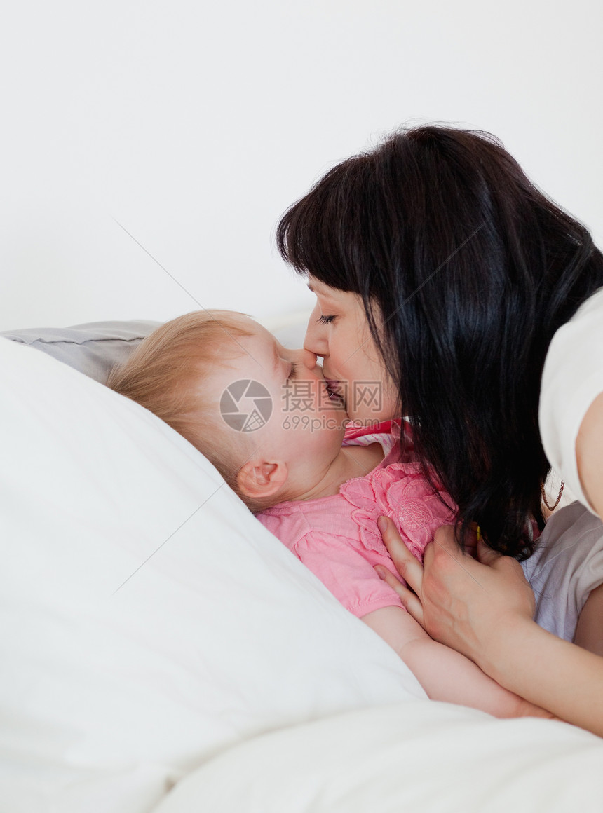 可爱的黑发美女 在床上亲吻她的孩子图片