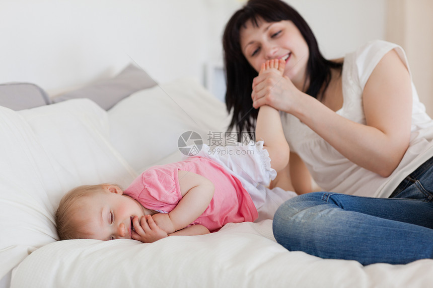 美丽的黑褐色女性美女在躺着时与婴儿玩耍图片