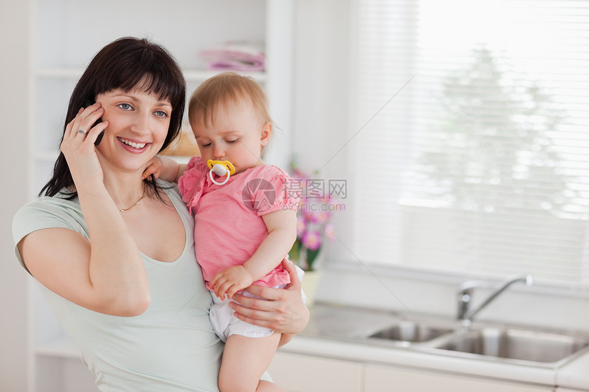 漂亮的女人在电话上 同时抱着孩子 在她的怀里图片