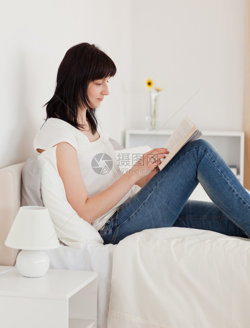 漂亮的黑头发女人坐在床上看书时在看书图片