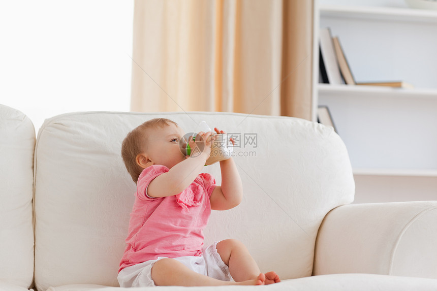 坐在沙发上时用奶瓶喂养可爱金发美女婴儿图片