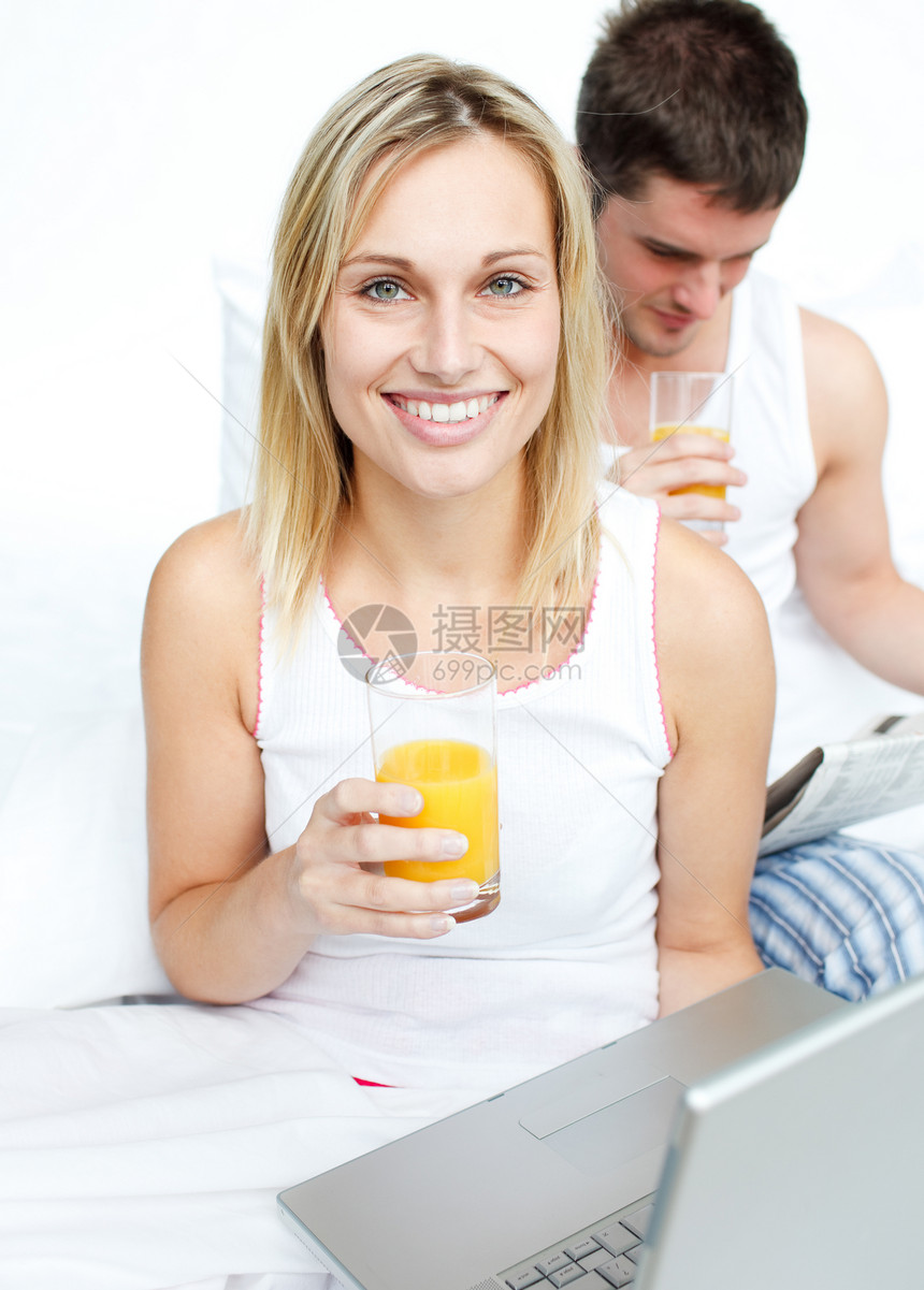 喝橙汁的女人和躺在床上看报纸的男人图片