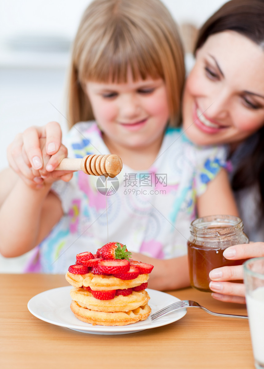 可爱的小女孩和妈妈 在华夫饼上加蜂蜜图片