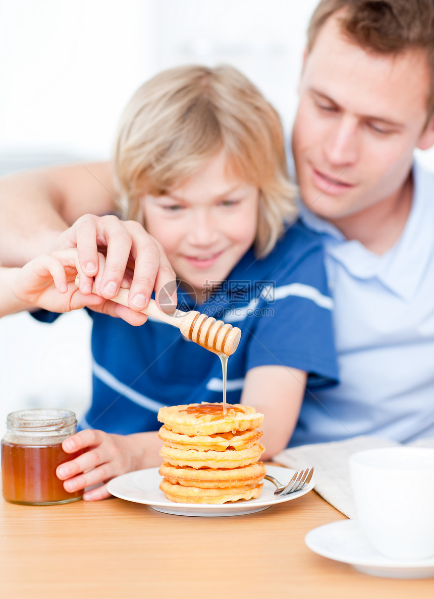 可爱的男孩和他父亲 把蜂蜜放在华夫饼上家庭孩子男生兄弟男人营养饼子童年微笑厨房图片