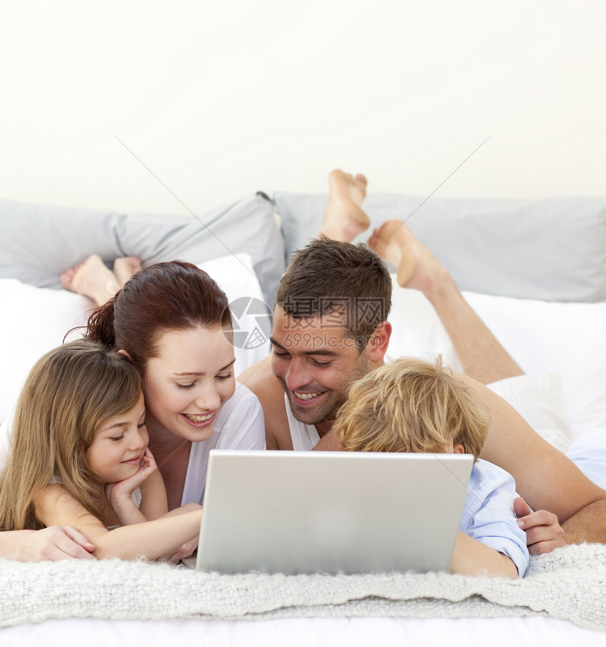 父母和在床上玩笔记本电脑的儿童图片