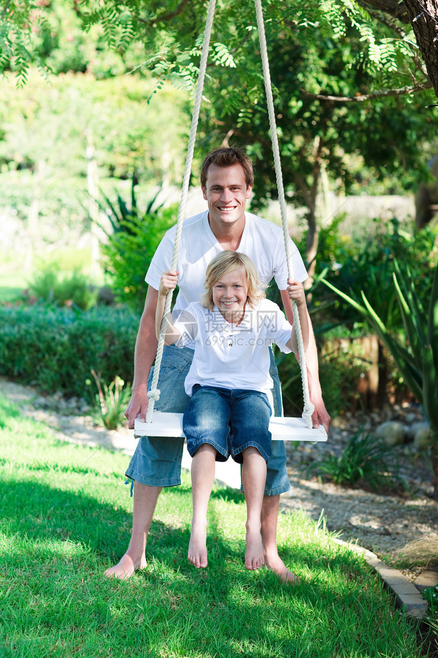 父亲和儿子在摇摆中晴天家庭微笑季节爸爸男生天空公园喜悦花园图片