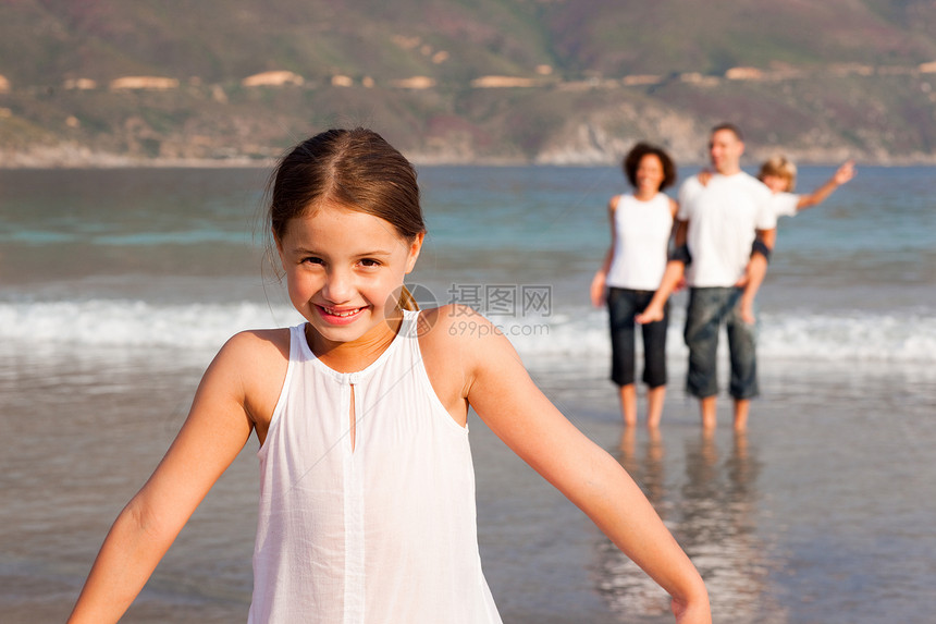 小女孩在沙滩上和她父母和背景兄弟的弟弟在一起图片