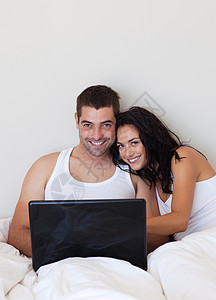 在卧室用笔记本电脑的一对漂亮的夫妻背景图片