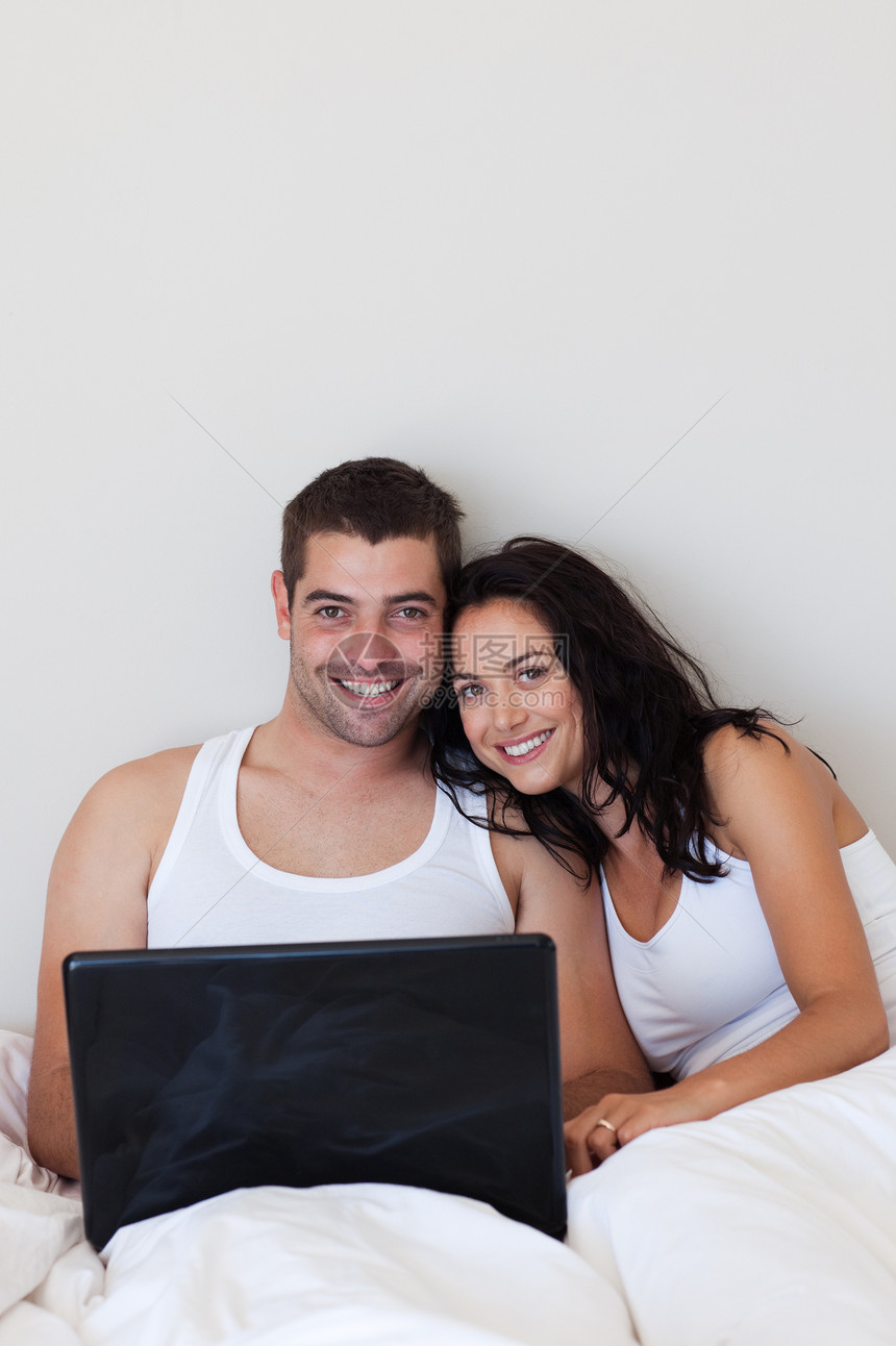 在卧室用笔记本电脑的一对幸福的情侣图片