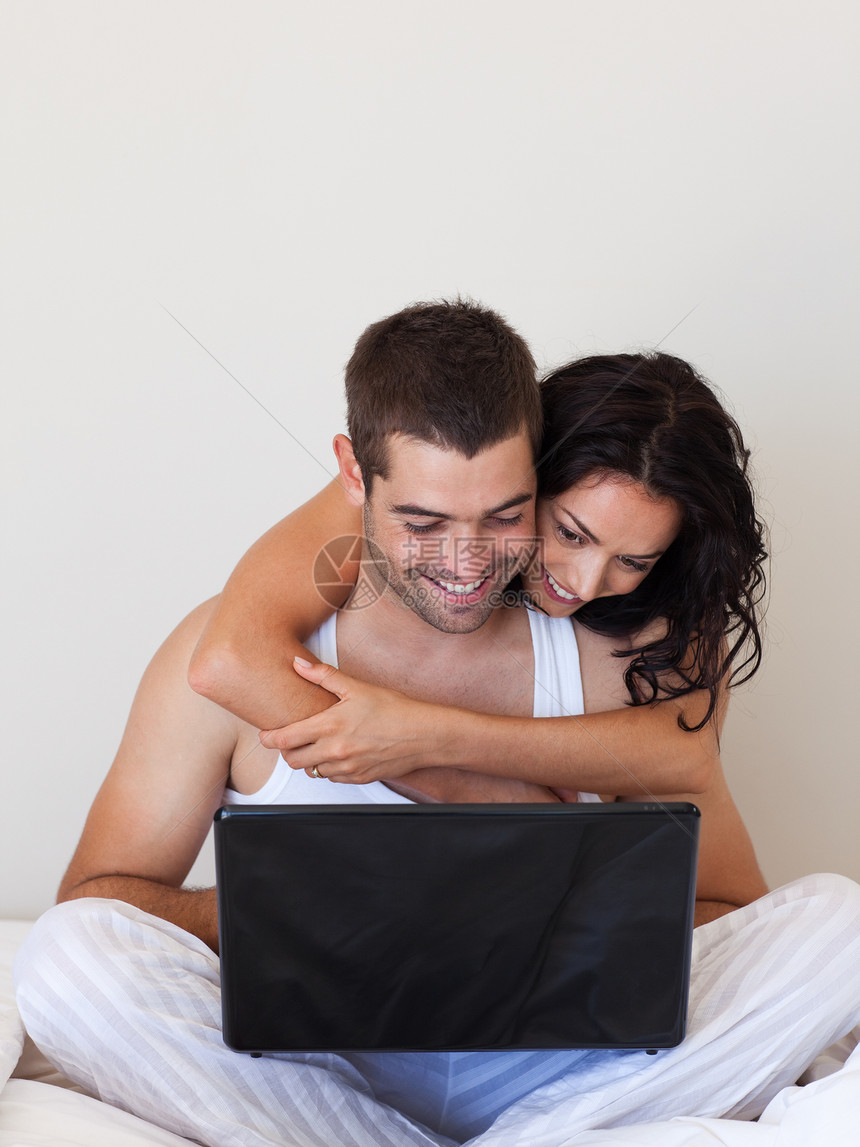 用笔记本电脑坐在床上的一对好夫妻图片