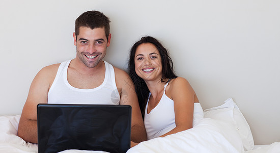 幸福的情侣在床上用笔记本电脑背景图片