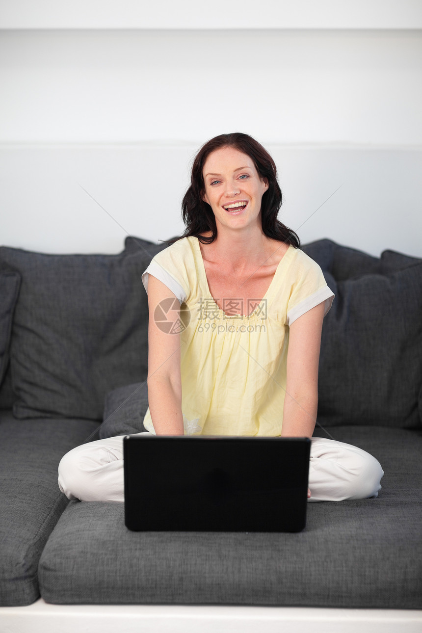 在灰沙发上使用笔记本电脑的笑女人图片