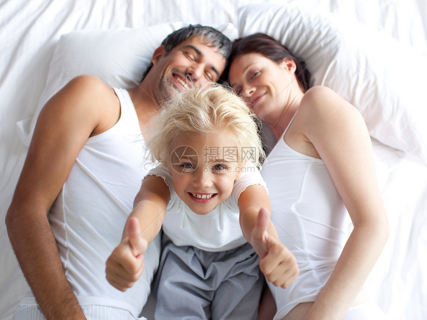 快乐的小女孩在床上 用拇指抬起她的父母图片