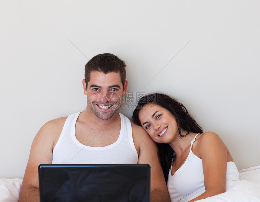 带着笔记本电脑坐在床上的一对情侣图片