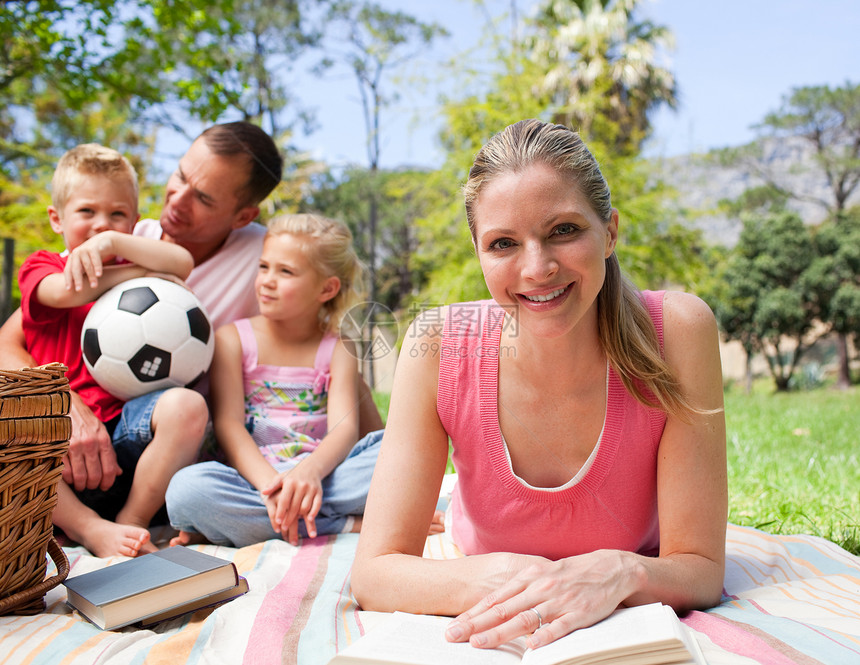 微笑的女人和家人一起在野餐上看书妈妈足球公园乐趣男性女孩孩子阅读父母女儿图片