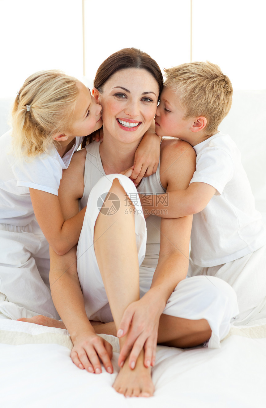 亲密的兄弟姐妹亲吻坐在床上的母亲和母亲图片