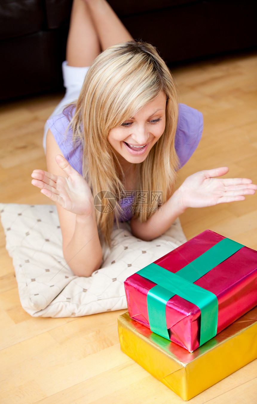 令人惊讶的年轻女子在客厅地板上打开礼物 开着礼物图片