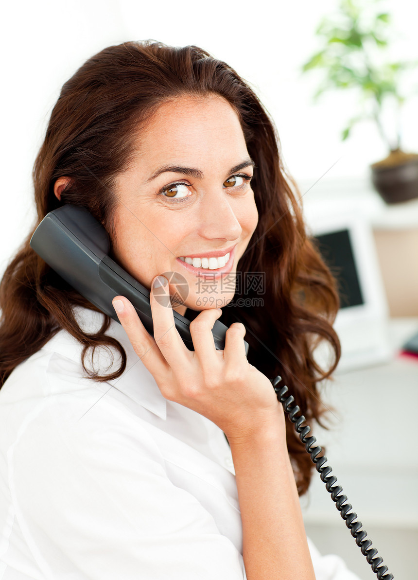 活跃的年轻商业女商务人士在她的办公桌旁通过电话交谈图片