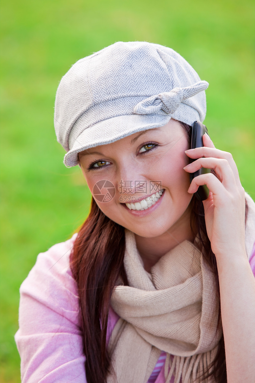 带着帽子和围巾在草地上讲电话的欢乐年轻女子图片