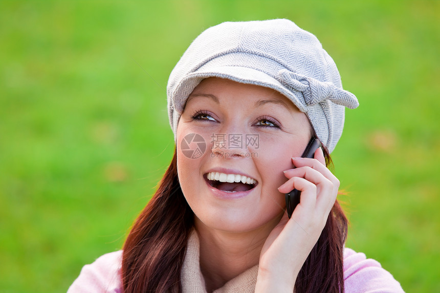 带着帽子和围巾在草地上讲电话的笑笑着年轻女子图片