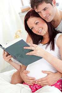 一位愉快的孕妇及其丈夫在阅读a b c d和背景图片