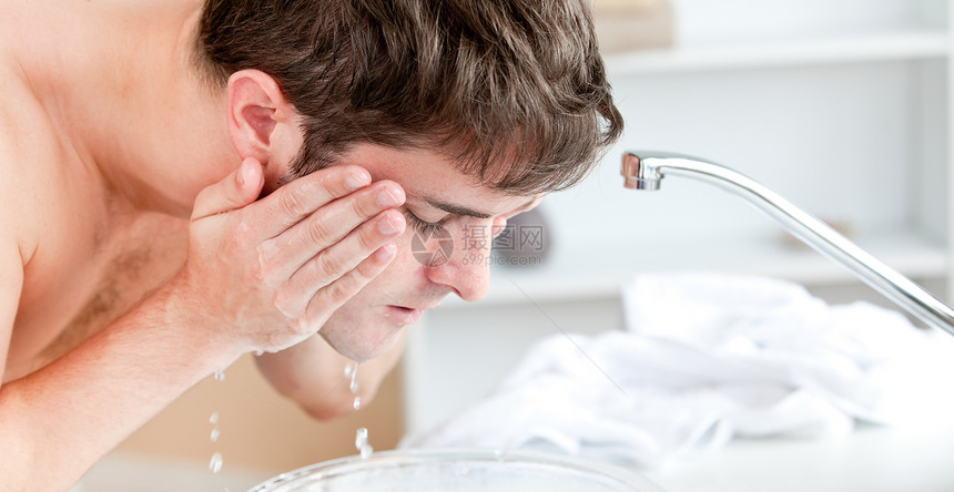 在刮胡子后 年轻高加索男子在脸上喷洒水图片