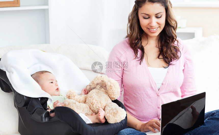 布莱亮的母亲在笔记本电脑上工作 她的孩子坐在旁边图片